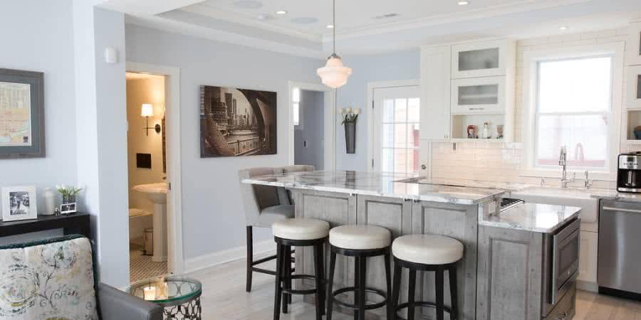 Remodeled kitchen with island with light gray cabinets, stone countertop, and bar stool seating.