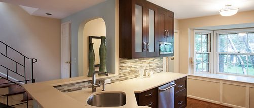 Remodeled kitchen with dark cabinetry and light countertops and multi-color backsplash
