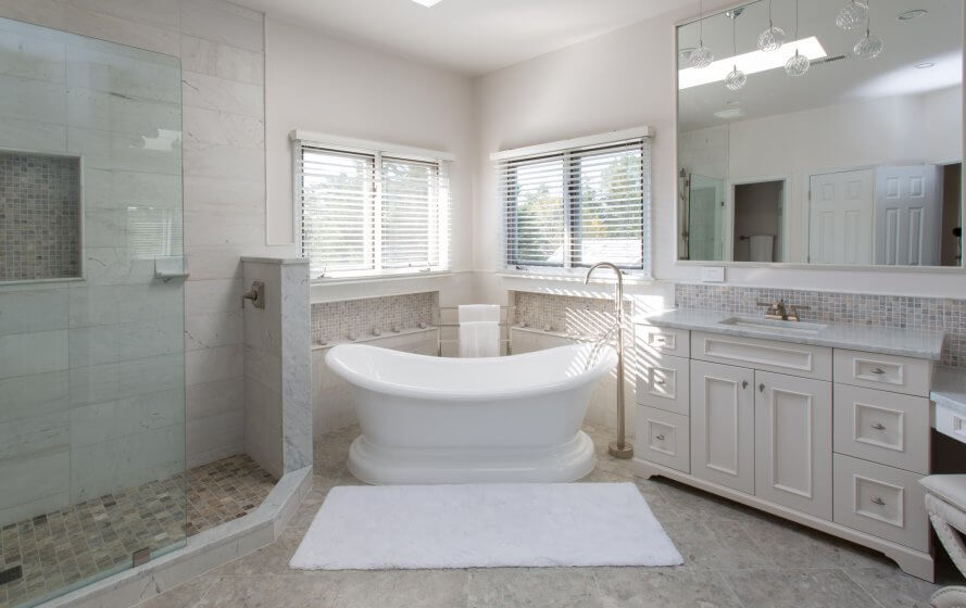 Remodeled bathroom with stand-alone soaking tub and walk-in shower. White tiles and white vanity.