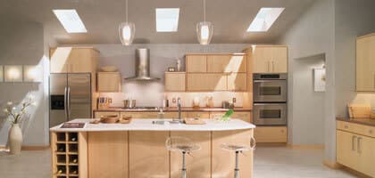 Bright, open kitchen remodel with pale woodgrain cabinets, recessed lighting, large island, and white floors.