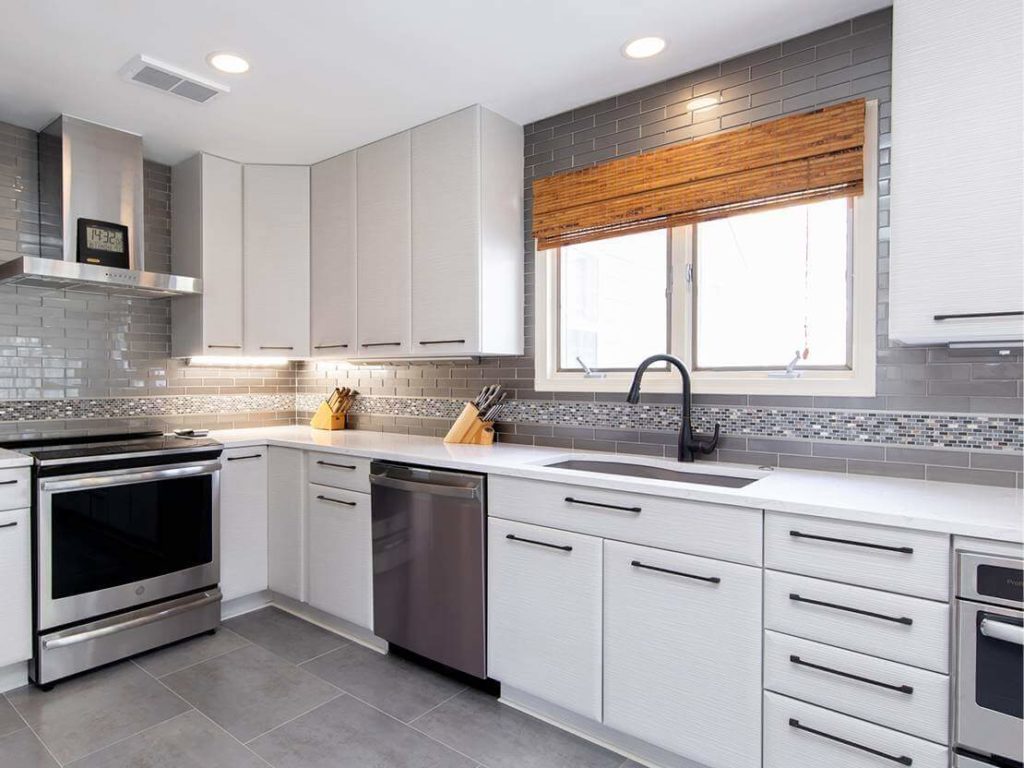 Modern kitchen renovation with white cabinets, gray tile walls, and white countertops.