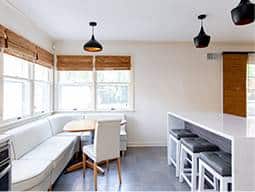 Kitchen with a white modern island and three black stools and a white corner booth.