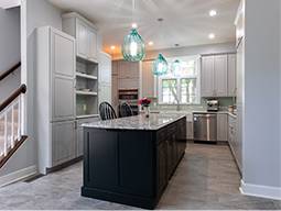Renovated home kitchen with a granite island and blue hanging chandeliers.