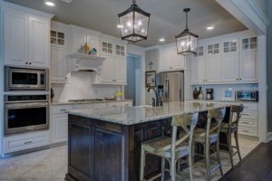 Remodeled kitchen with white cabinets, large island, stone countertops, and pendant lighting.