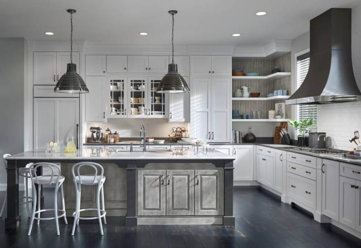 Remodeled kitchen with an island and white cabinets and gray island base. Dark wood floors, stainless steel pendant lights and vent hood.