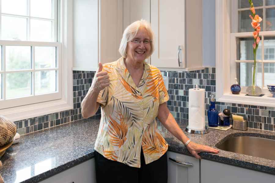 an older woman standing in a kitchen giving the thumbs up