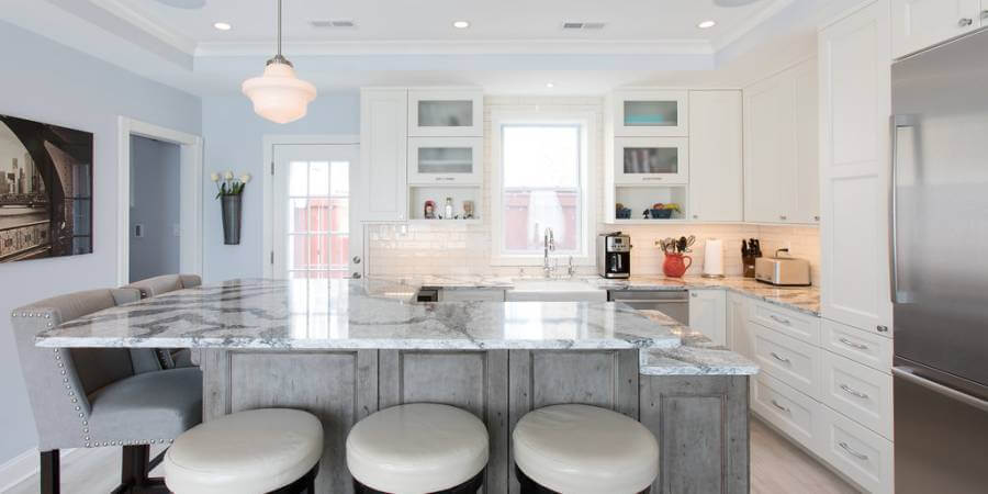 Light and bright kitchen with island, white cabinets, and stone countertops.