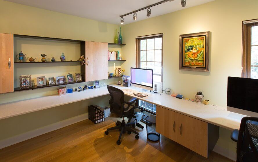 home office addition with built-in desk along two walls, built-in shelving on one wall, and track lighting above part of the desk. Wood floors.