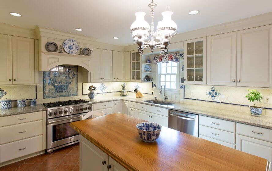 Custom kitchen remodel with French tile backsplash, white cabinets, brown tile floors, butcher-block topped island, pendant light and recessed lighting.