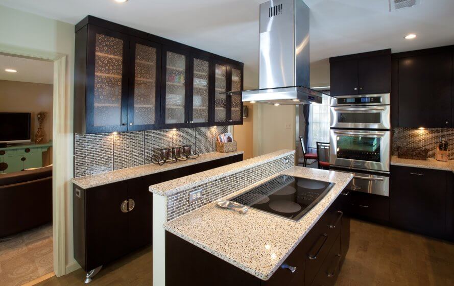Custom kitchen remodel with dark cabinets, light stone countertop, and glass tile backsplash.