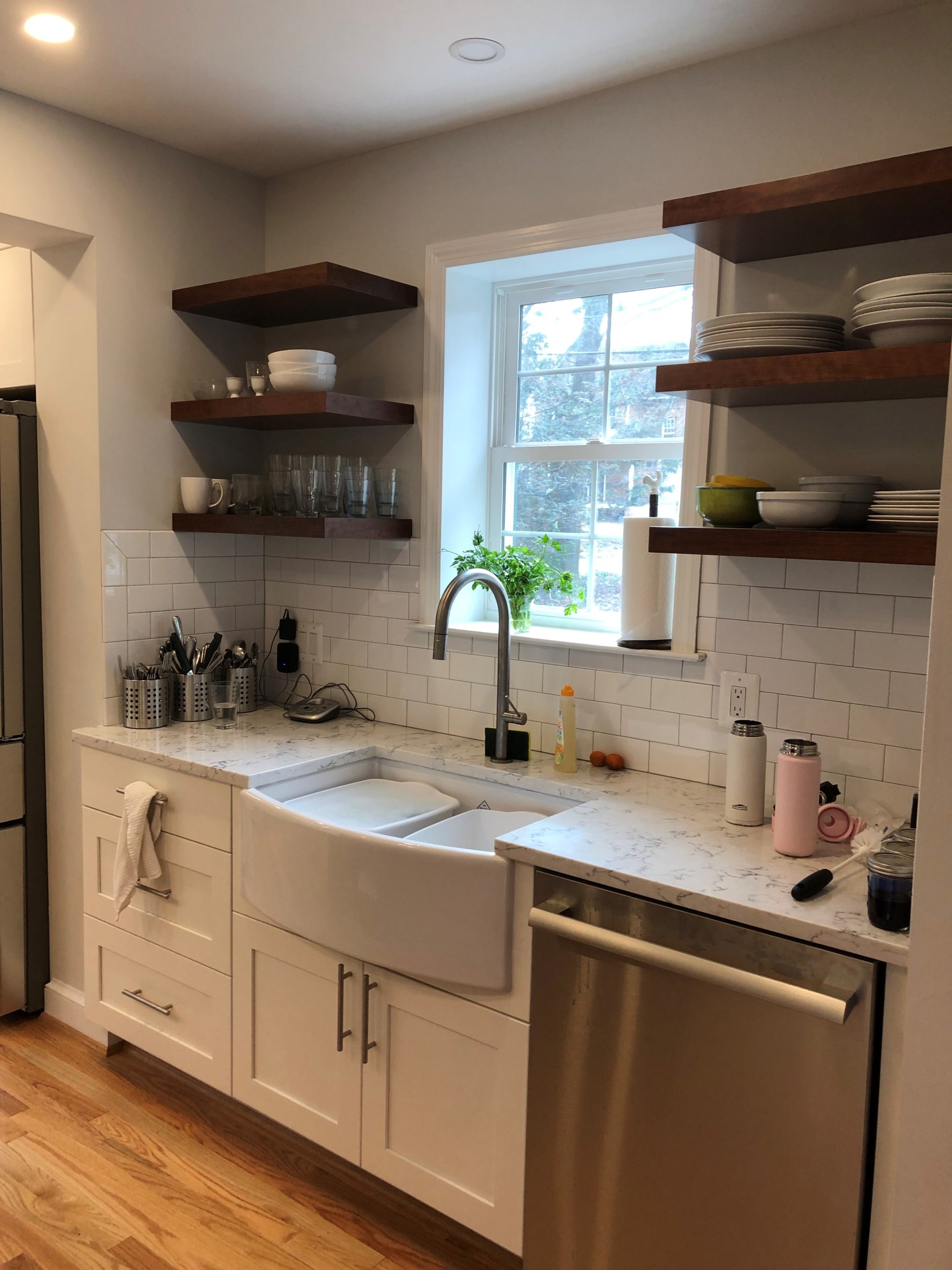 a kitchen with white cabinets and wooden floors, with open wooden shelving above countertops