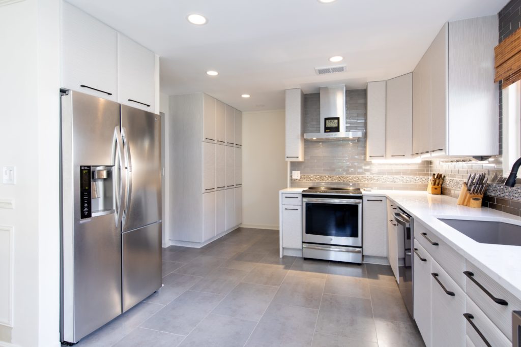 Newly designed kitchen with light gray floors, white cabinets and counters, and stainless steel appliances.