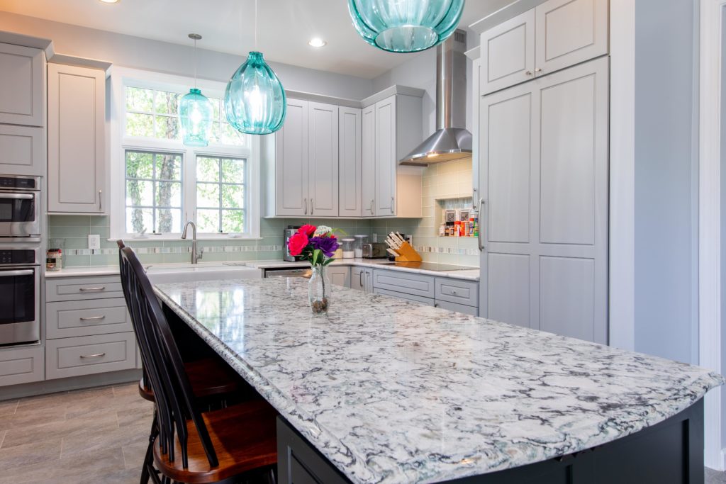 Remodeled kitchen with large island, granite countertops, white cabinets, and teal pendant lights.