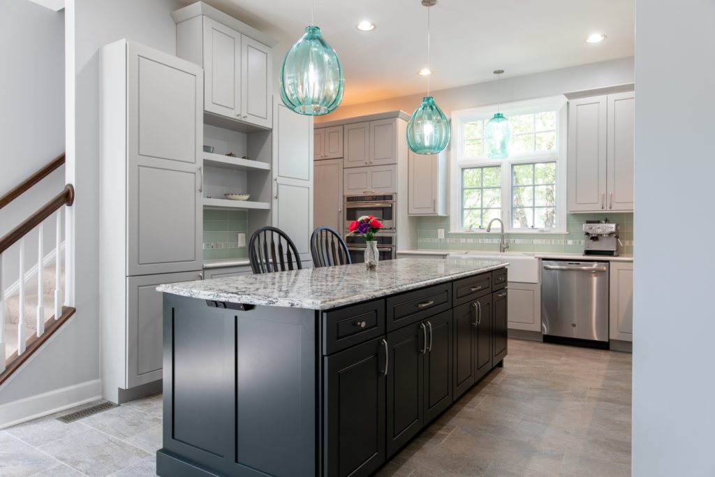 Remodeled kitchen with stone countertops, dark island cabinets, teal pendant lights.