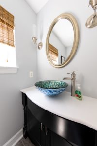 Remodeled bathroom with black vanity and white countertop and unique blue sink.