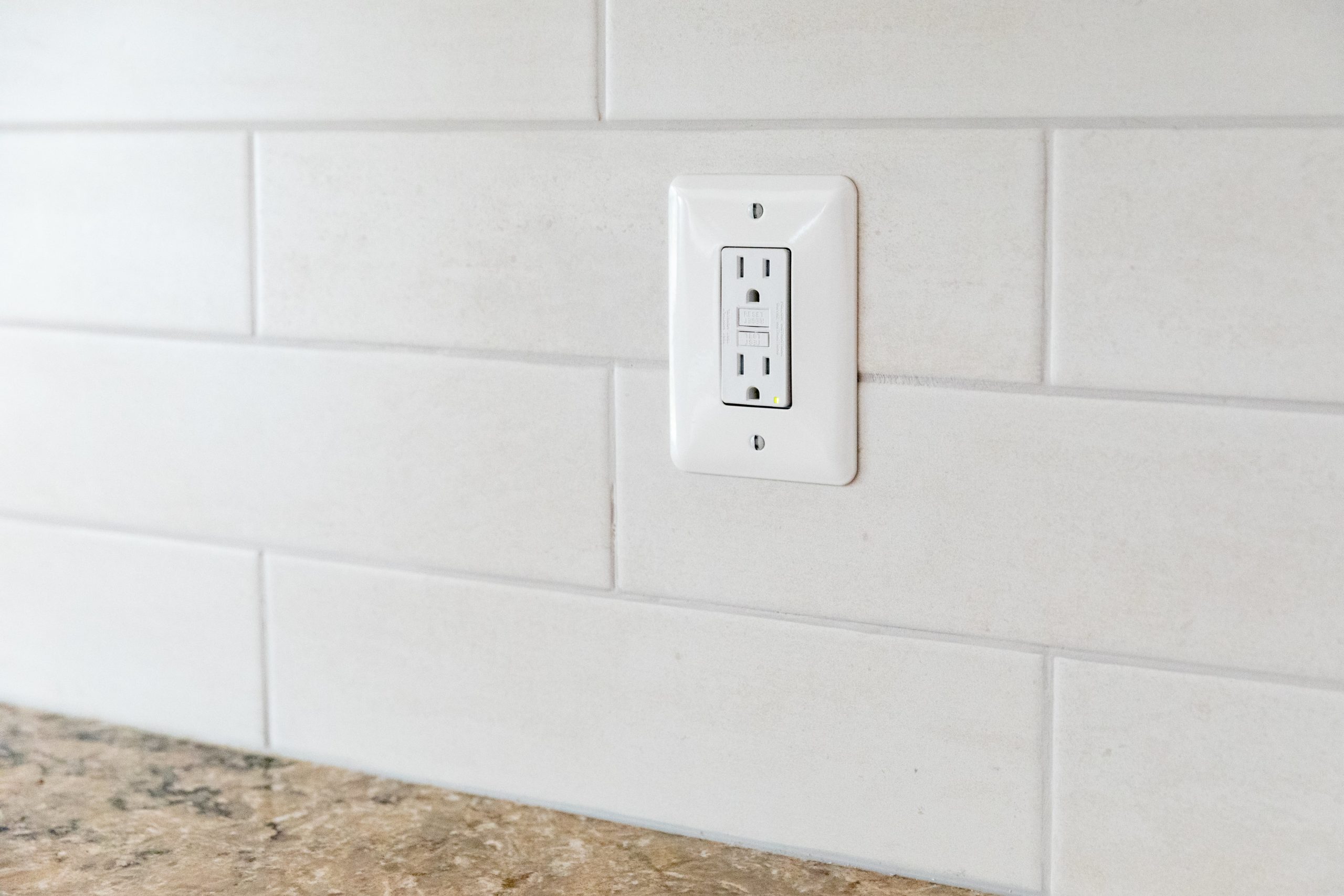 an outlet on a white tiled wall