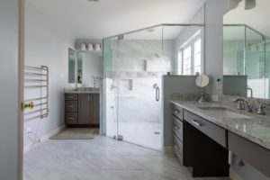 Remodeled bathroom with white stone floor and glass-enclosed shower.