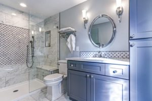 Remodeled bathroom with new shower, blue cabinets, and round vanity mirror.