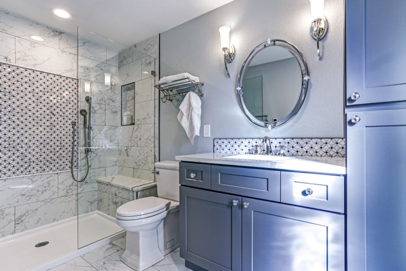 Remodeled bathroom with blue cabinetry and glass stand-in shower enclosure