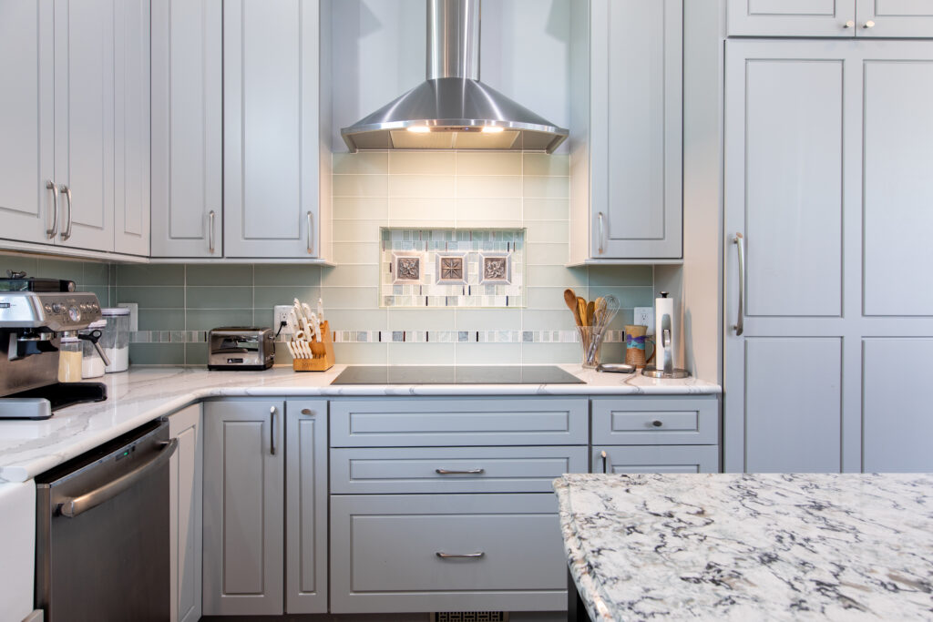 A remodeled kitchen with marble counter tops and light gray cabinets.